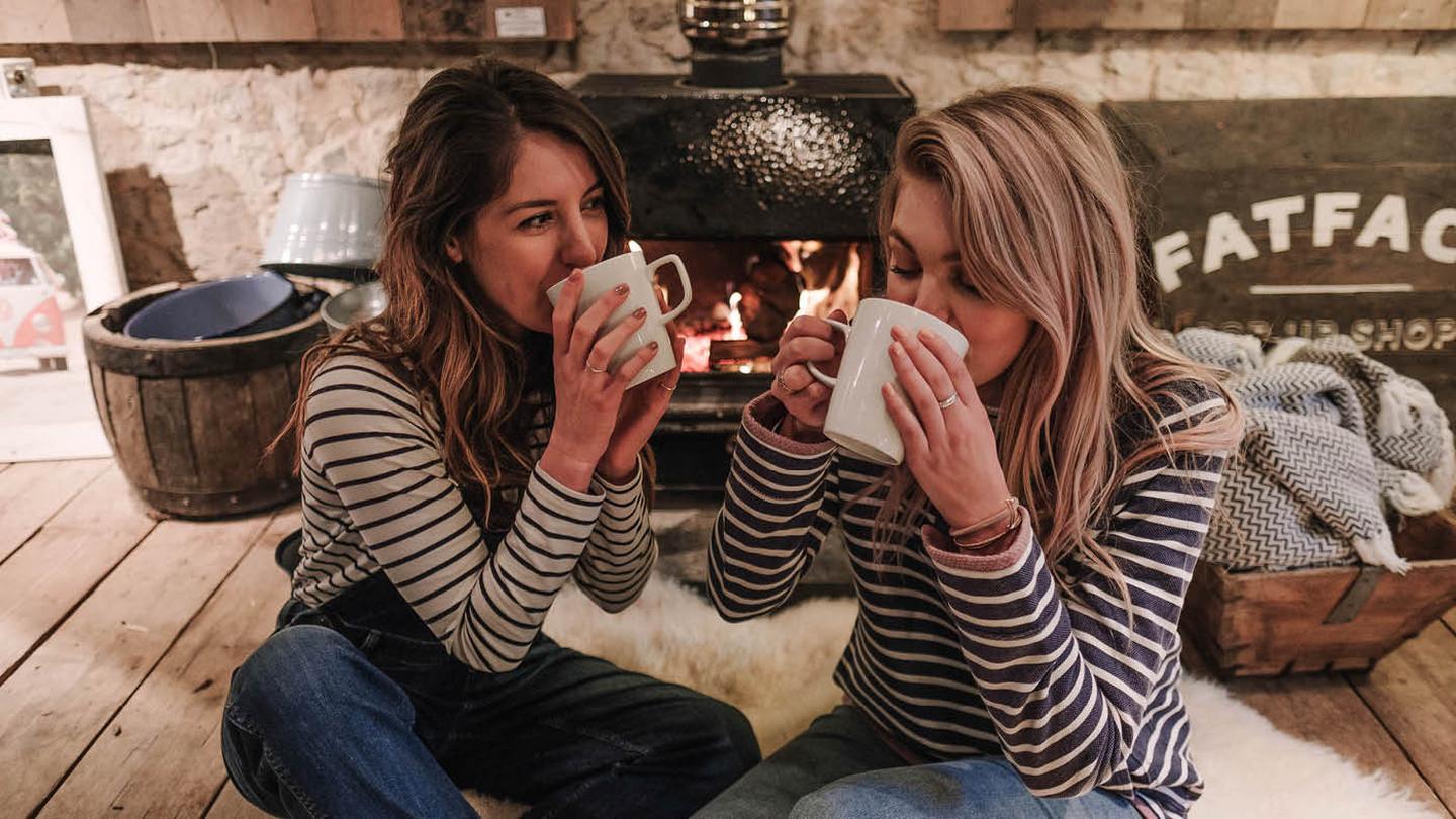Immy and Fifi wearing stripe tops, sitting in front of the fire wearing hot drinks.